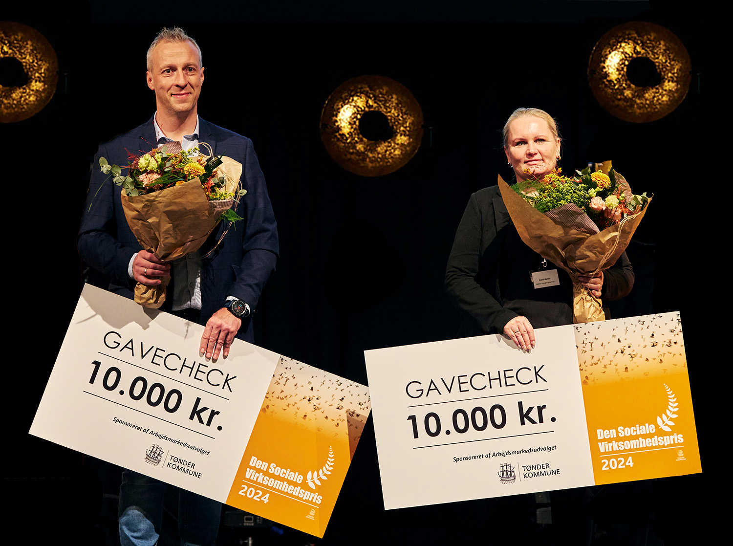 En mand og en kvinde med blomster og hver en gavechek på 10.000 kroner