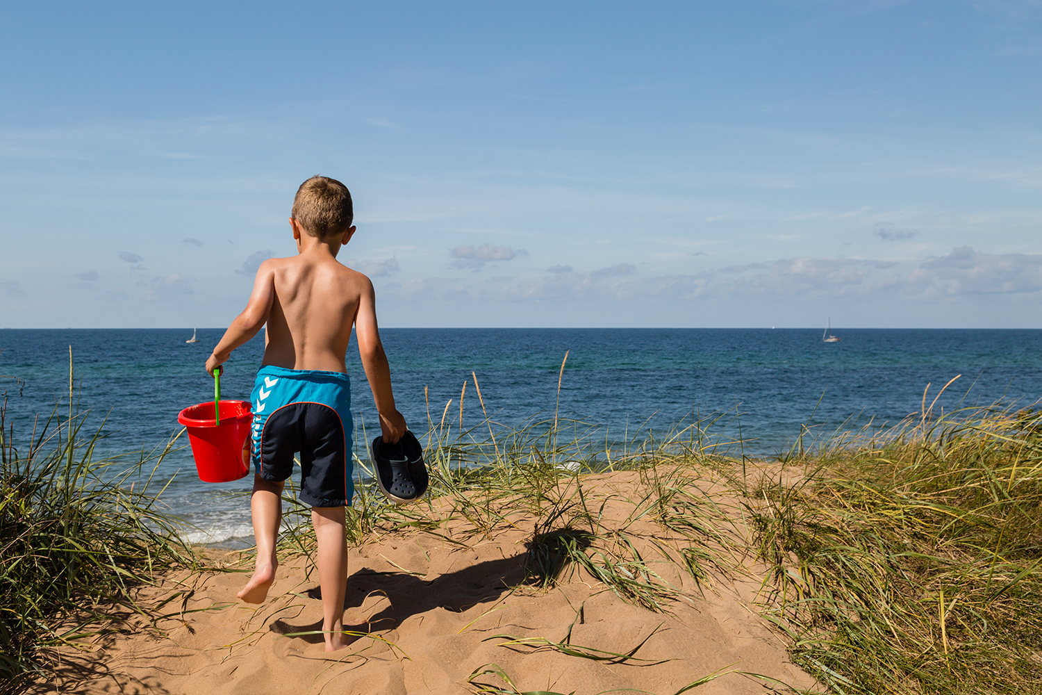Dreng i badeshorts, der står og kigger ud over vandet 