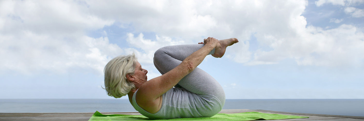 Ældre kvinde der dyrker yoga på en badebro