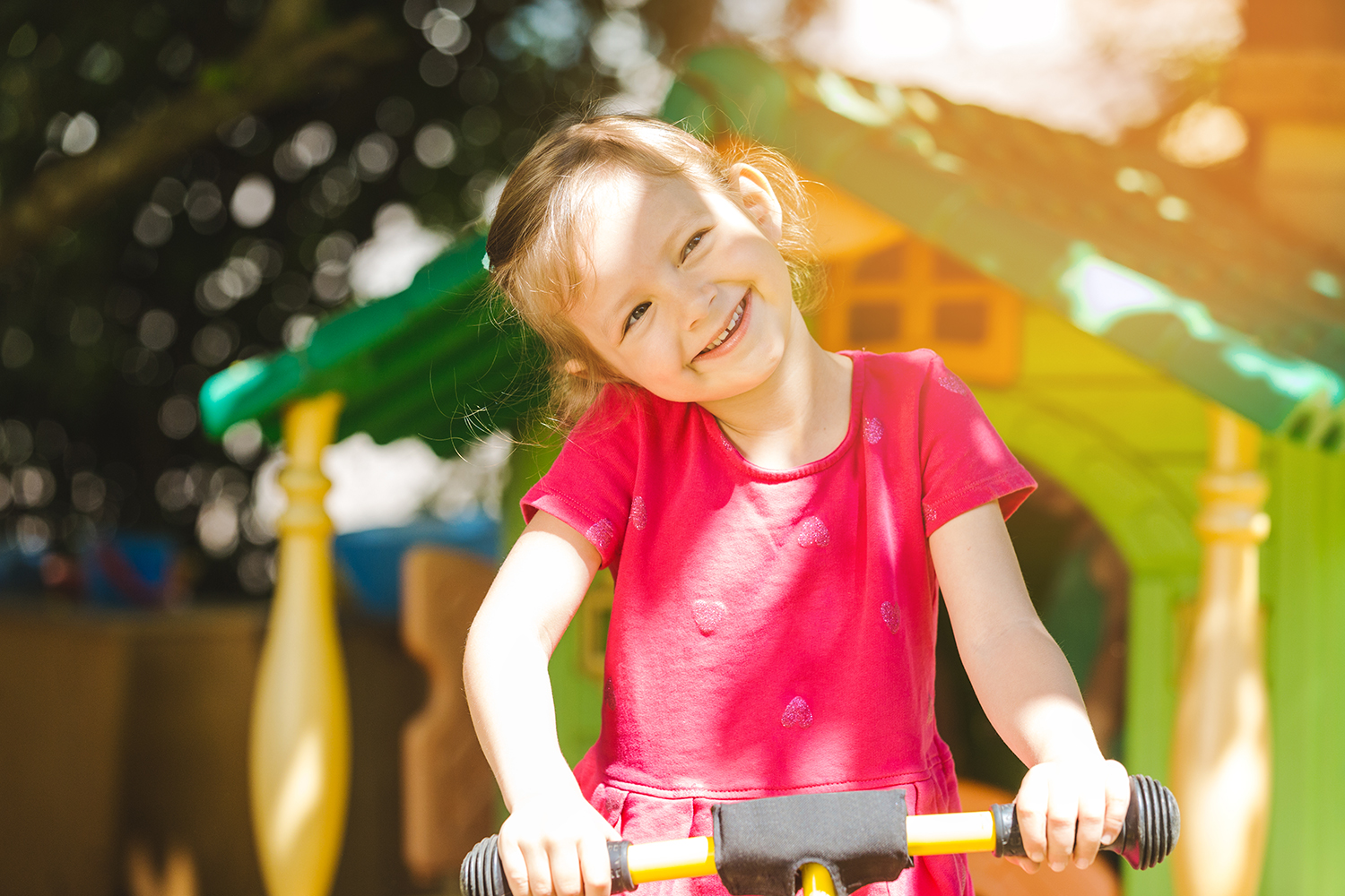 Pige der står og holder ved hendes cykel, i baggrunden ses et legehus