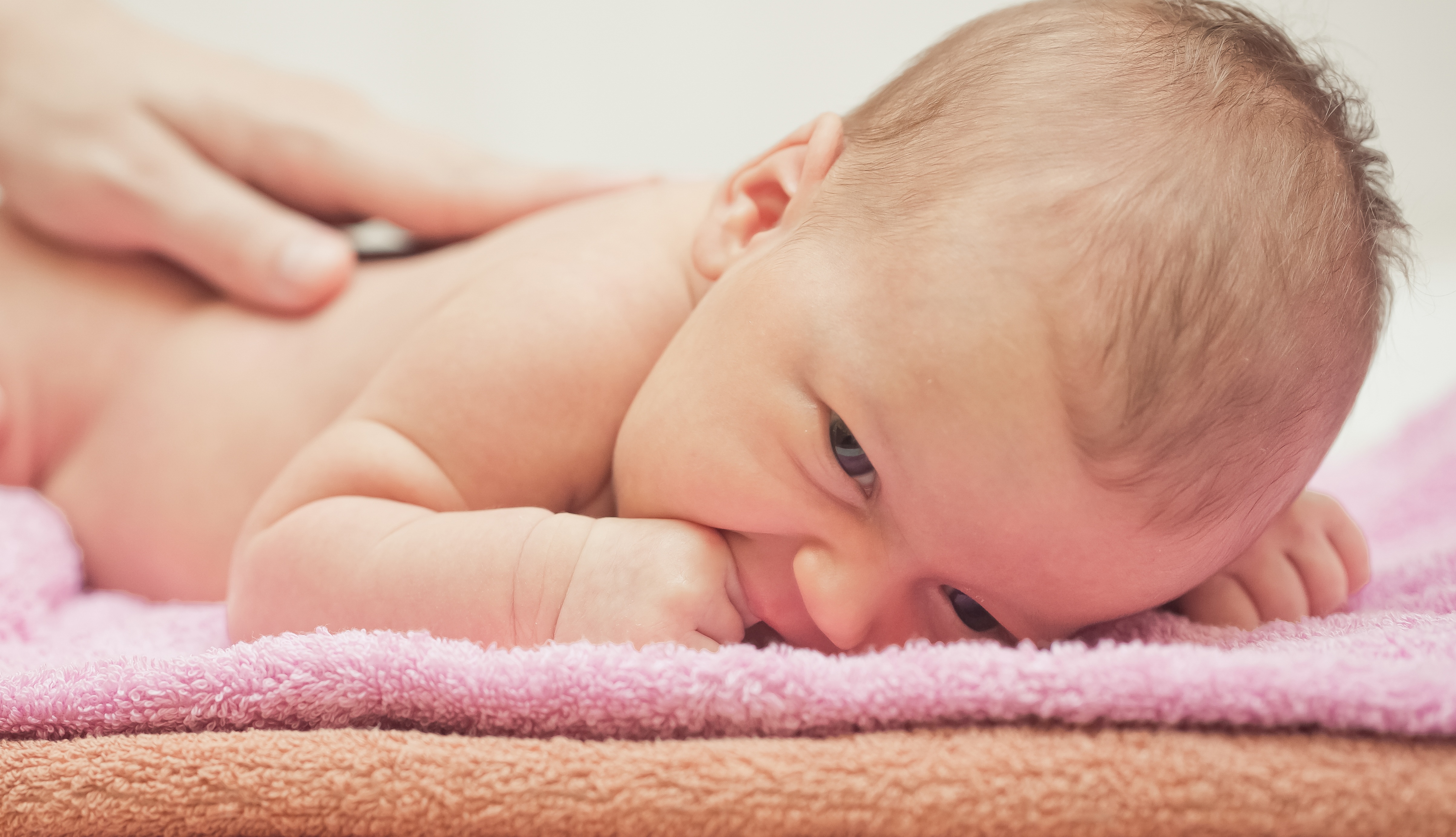 Baby der ligger på et lyserødt håndklæde og får massage